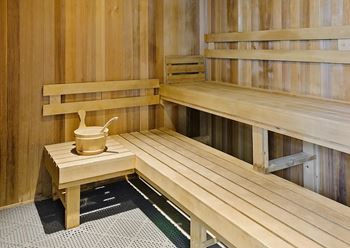 A wooden sauna with a bench and a bucket on a table.